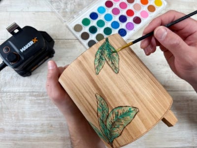 image of a person painting the wood burned design with green paint