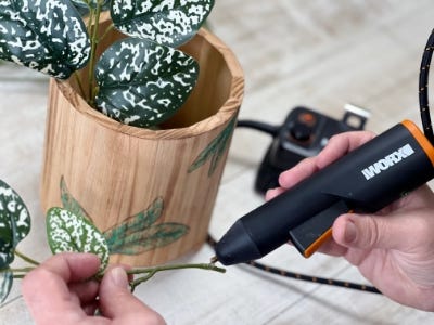 person hot gluing the plant stems to the foam