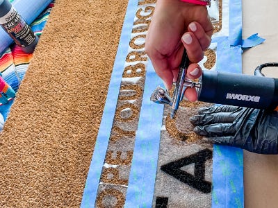 Spraying airbush paint onto doormat for letter A