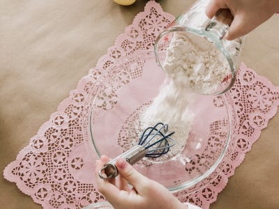 Pouring flower into bowl with wisk on top of pink placemate 