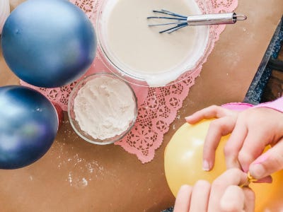 Two blown up blue ballons next to mixed flour and water while yellow ballon is being blown up