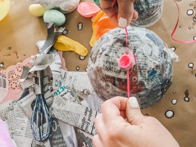 Hands tying ribbon around the end of blown up ballon that newspaper surrounding it