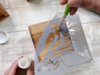 applying embossing glue to stencil and wood piece