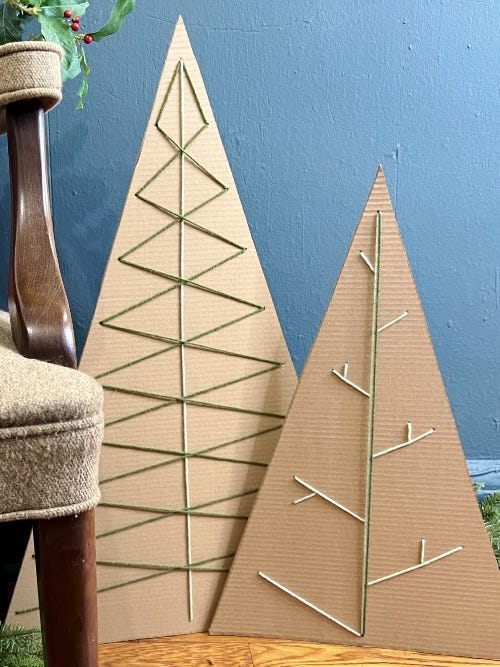 two cardboard christmas trees on a table decorated with green and white yarn