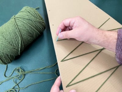 threading yarn through holes half way up cardboard piece