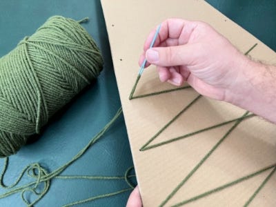 threading yarn through holes half way up cardboard piece using threading tool