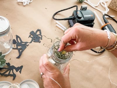 stuffing greenery into jar with lights