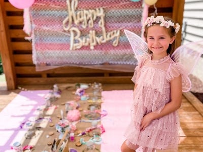 girl in pink dress in front of arts and crafts and happy birthday sign