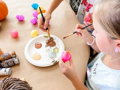 girl using paint brush with brown color on pink egg