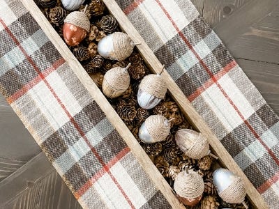 multiple twine decorative acorns laying in wooden basket on top of plaid table cloth