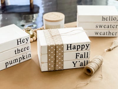 3 faux stacked books with lettering on them next to yarn roll