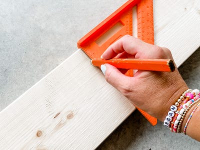 writing with pencil and using 90 degree measuring ruler on wood board