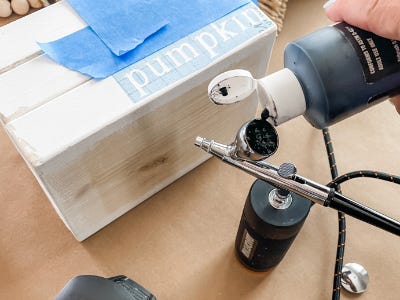 pouring paint into airbrush next to stenciled wood blocks