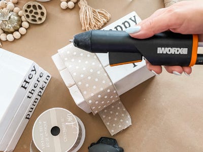 holding hot glue gun over ribbon and three stacked wood blocks