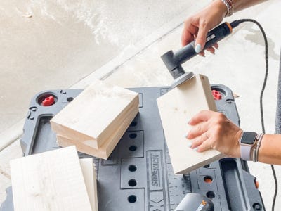 holding the angle grinder and using the tool to grind down the corners of wood block thats on worx table 