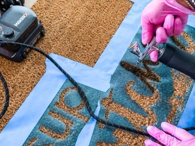 using airbrush to paint the words onto doormat