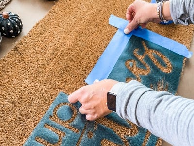 Laying blue masking tape around stencil onto dormat