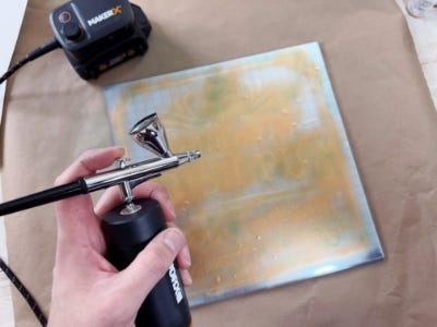 air brush being used to spray paint over stencil into mirror piece