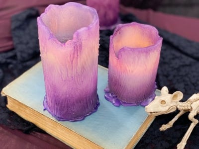 lighted purple color candle 2 different sizes and one on box next to skeleton mouse