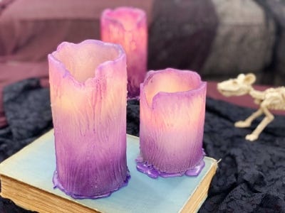 lighted purple color candle 3 different sizes and one on box next to skeleton mouse