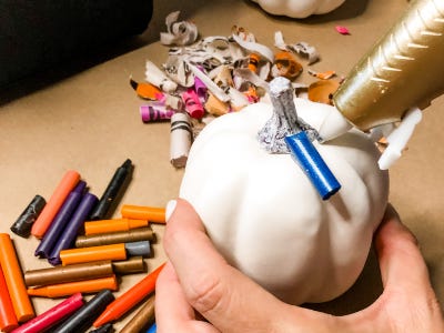 using glue gun to glue blue color crayon on top of white pumpkin