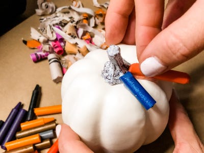 placing orange color crayon on top of white pumpkin