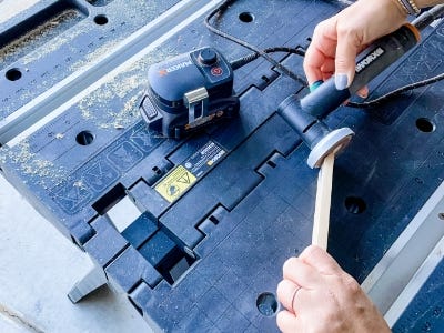 image of a person using the MakerX angle grinder to sand the end of the piece of wood