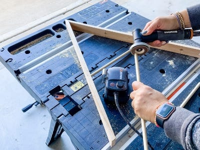 image of a person uising the MakerX angle grinder to sand the edge of a wooden dowel with the wooden triangle on the work table