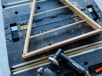 image of the wooden dowels places into the wooden triangle and the MakerX angle grinder laid next to it on the work table