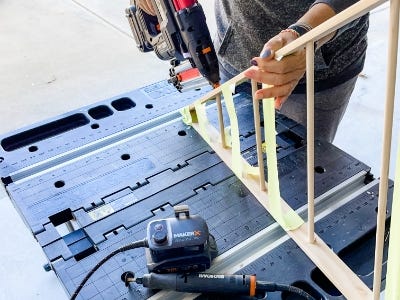 image of a person using a Worx Nail Gun to hold the dowlels in place on the wooden triangle on top the work table