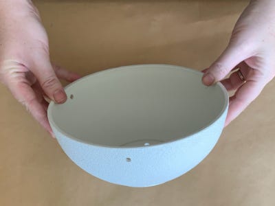 holding white pot with 3 small holes in it