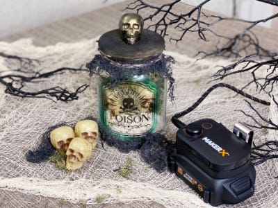 spooky posion jar next to battery and charger and 3 skeleton heads