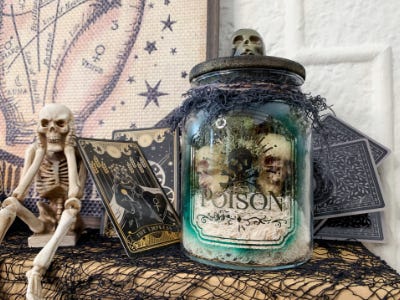 spooky posion jar on table next to skeleton man and cards