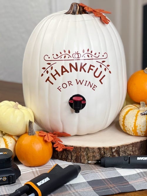 white pumpkin on a table with the word Thankful painted on and dispensing wine surrounded by smaller pumpkins