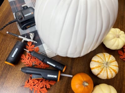 air brush and mini glue gun next to large white pumpkin next to little pumpkins