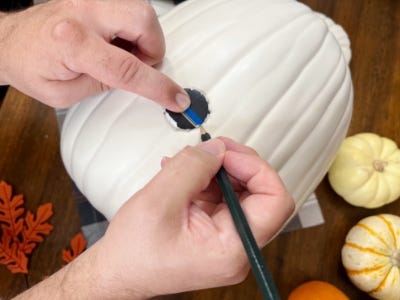 pencil cutting out small circle on white pumpkin