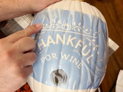 placing stencil of thankful for wine on white pumpkin