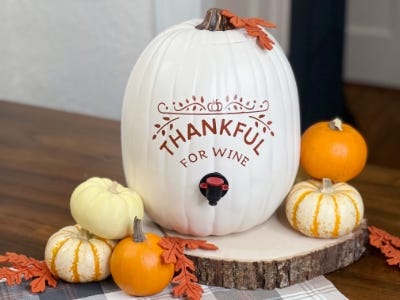 white pumpkin wine dispenser with thankful for wine and smaller pumpkins next to it