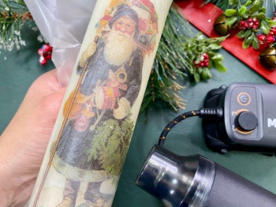 using heat gun to apply santa sticker to candle to stick