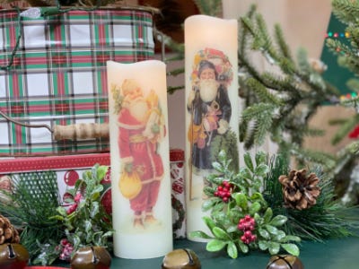 two santa candles standing to next to eather and greenery