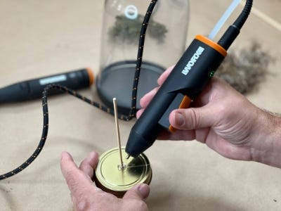 glue gun gluing skewer into hole of cap