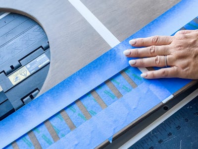 placing two blue painters tape above and below stripe painters tape onto stained plywood board