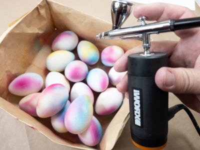 person adding pink paint to the eggs in a box with the worx maker x air brush