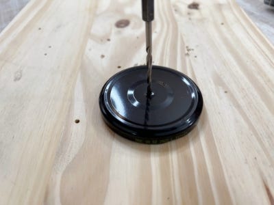 using rotary drill drilling hole into top of black jar lid