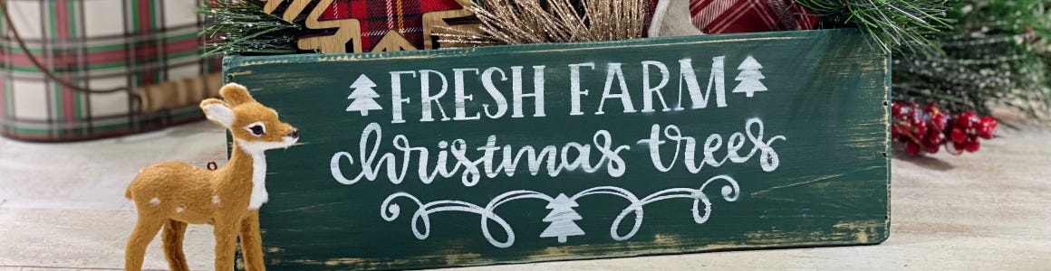 Fancy script font of fresh farms Christmas trees on green wood crate next to reindeer 