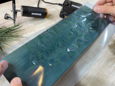 Clear stencil being applied to green painted side of wood block