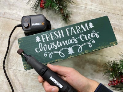 rotary tool being held in front of painted white and green wood block with words on it