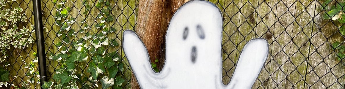 spooky ghost painted wood cut out in front of fence