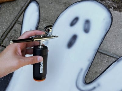 airbrush being held in front of white and black painted plywood ghost