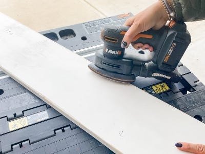 using sander to sand down the wood board on top of worktable